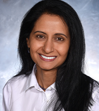 Black-haired woman with loose hair wearing a doctor's coat looking and smiling at the camera