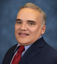 close-up of a man in a black suit with a blue shirt and red tie