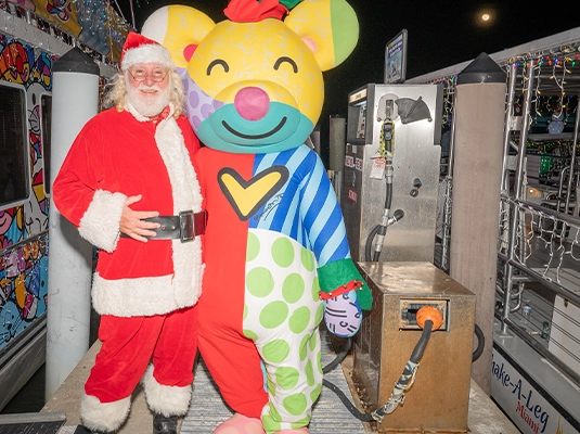 Person dressed as a colorful bear next to person dressed as Santa Claus