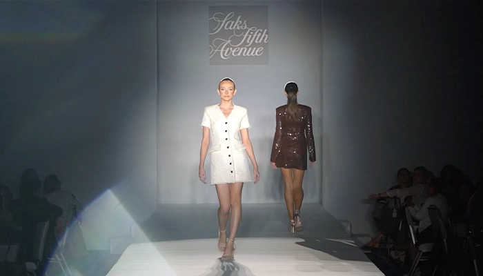 Two women walking in front of several people on a runway.