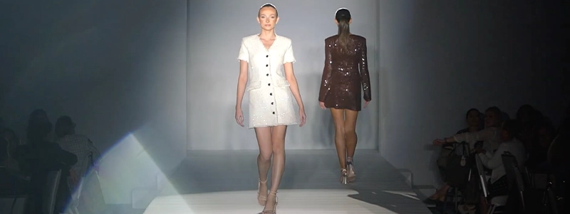 Two women walking in front of several people on a runway.