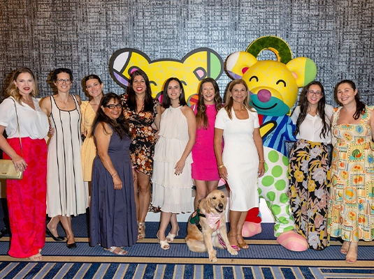 A large group of women wearing dresses, posing and smiling at the camera.