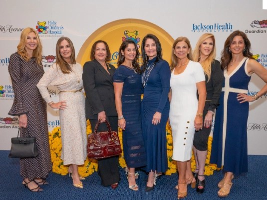 Group of elegantly dressed women, posing and smiling at the camera during an event