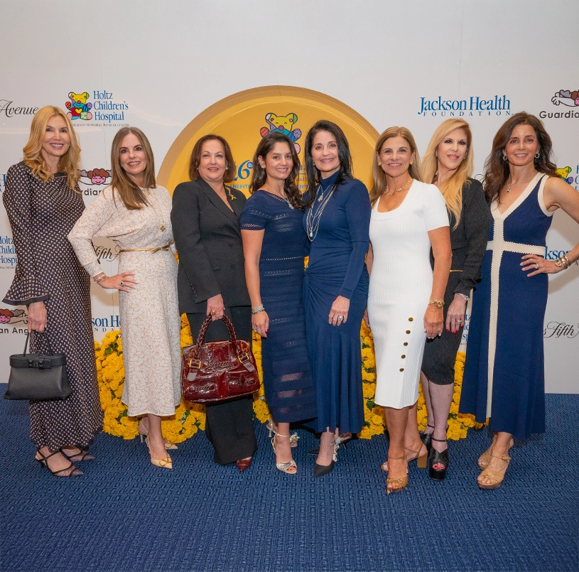 Group of elegantly dressed women, posing and smiling at the camera during an event