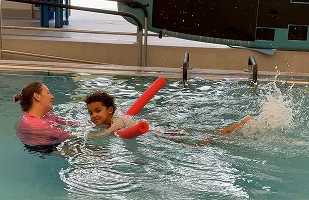 child playing in the pool next to a woman
