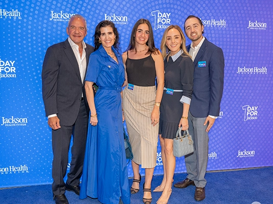 Five people dressed in suits posing and smiling at the camera during an event.