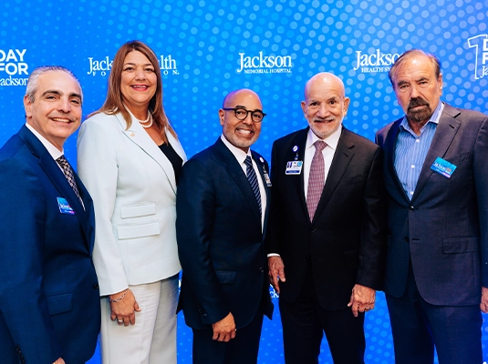 Five people dressed in suits posing and smiling at the camera during an event.