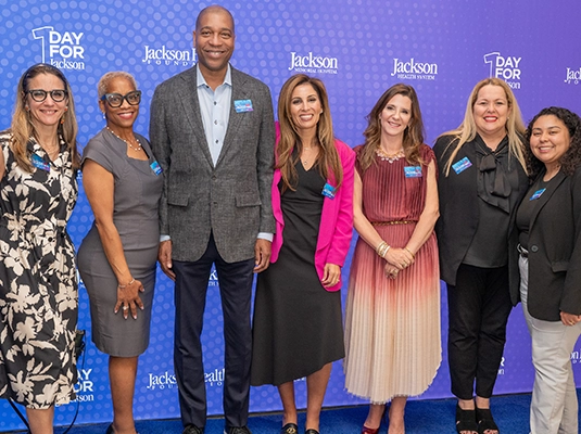 Seven people dressed in suits posing and smiling at the camera during an event.