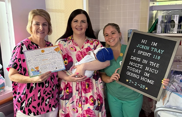 Three women holding a sign and lifting a baby.