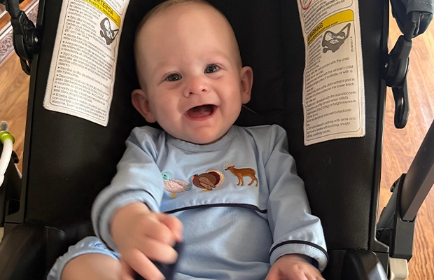 A baby smiling at the camera, sitting in a stroller.