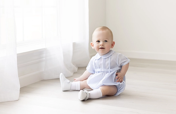 A baby sitting on the floor, wearing blue clothes.