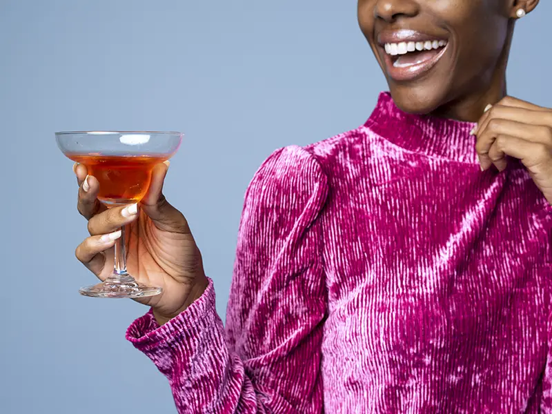 A closeup of a woman smiling, she is holding a drink and wearing a pink outfit