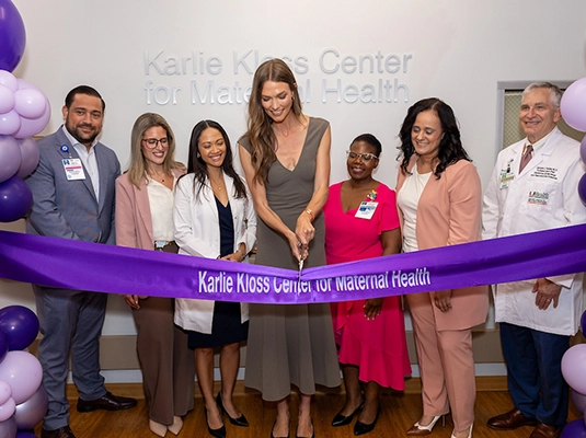 A woman cutting a purple ribbon in front of several people.