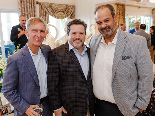 Three men embracing and smiling at the camera.