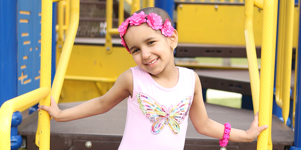 Salma in a playground smiling, she is wearing a pink ballet dress and a flower crown