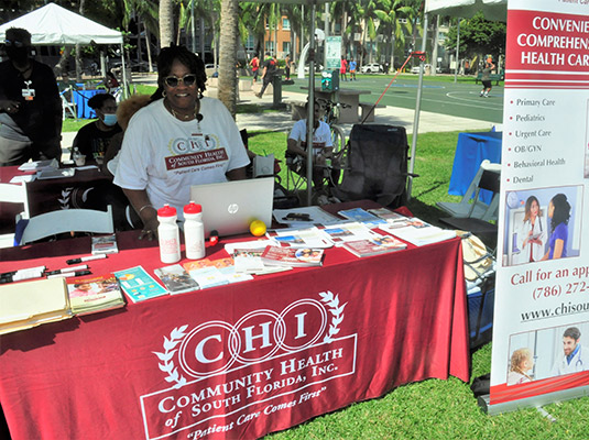 A woman behind a red booth that reads Community Health of South Florida, Inc.