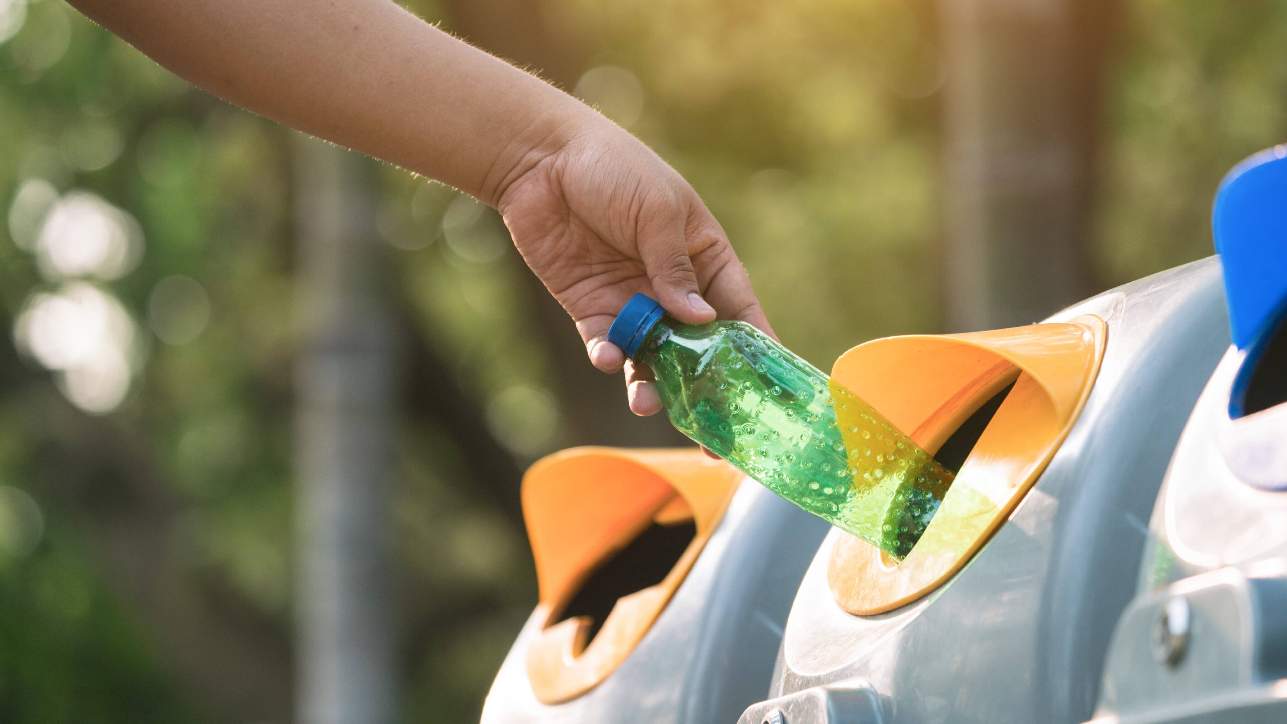 Hand placing used plastic bottle in its recycling bin.