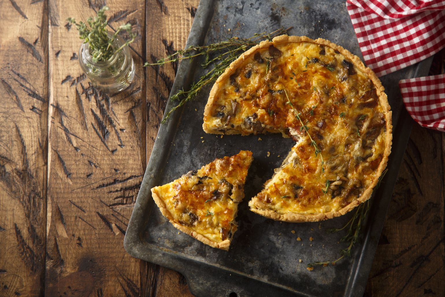 Quiche de frango com fatia cortada, aromatizada com tomilho, sobre tabuleiro de forno.