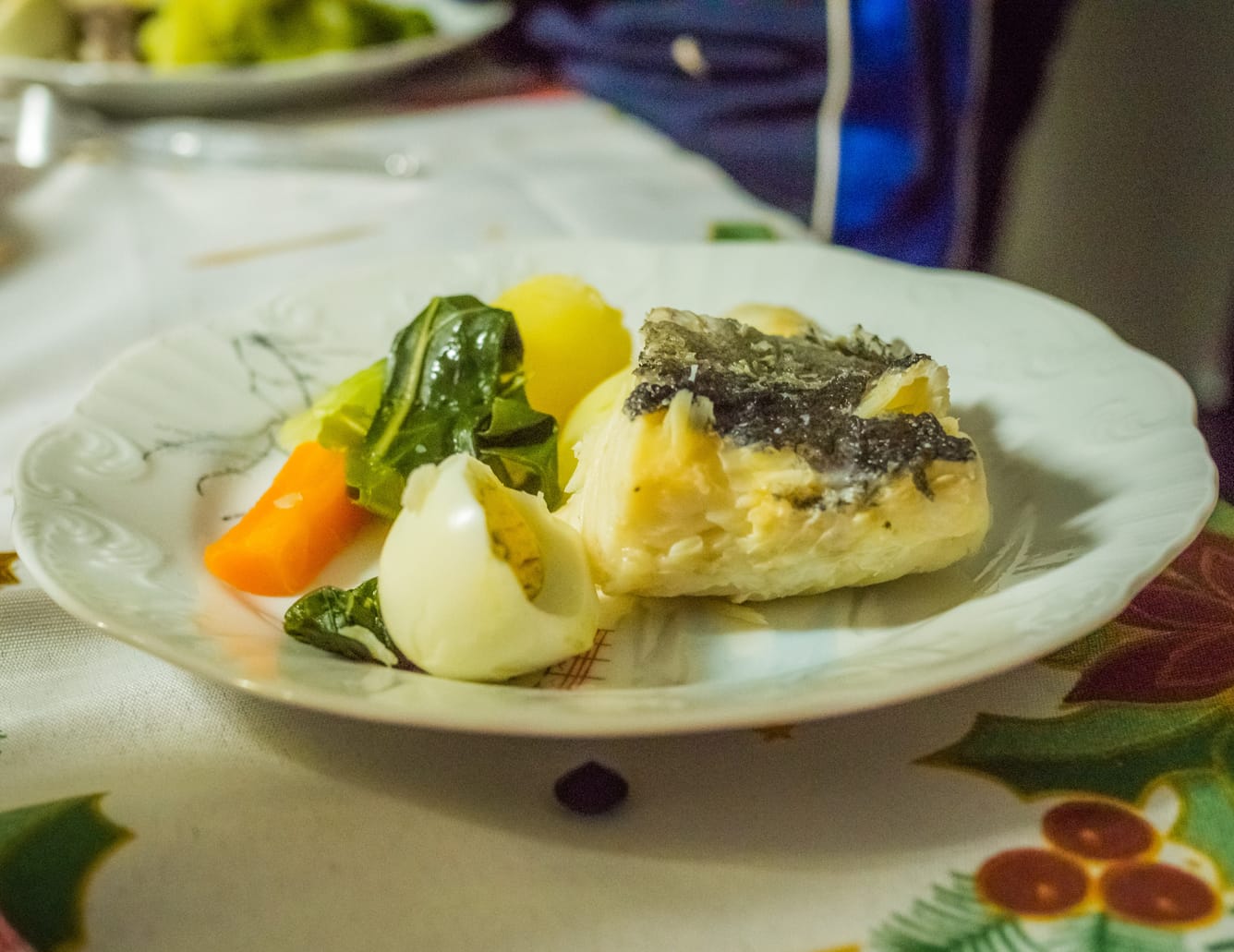 Patro de bacalhau acompanhado com batata, couve, cenoura e ovo cozido sobre mesa com toalha de linho.