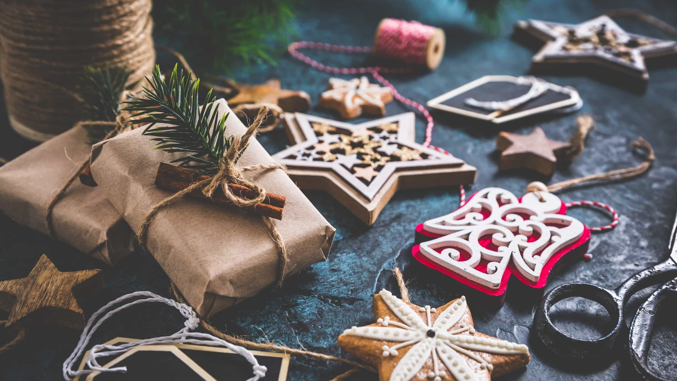 Presentes embrulhados com papel Kraft e decorados com paus de canela e azevinho, em mesa com decorações para árvore de Natal.