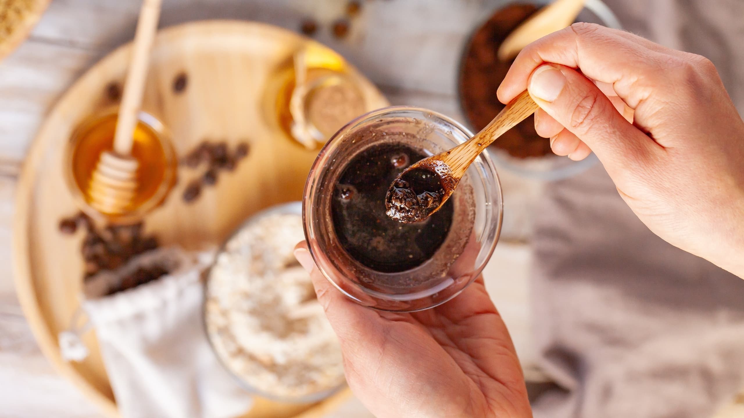 Woman's hand mixing a coffee scrub in a glass bowl.