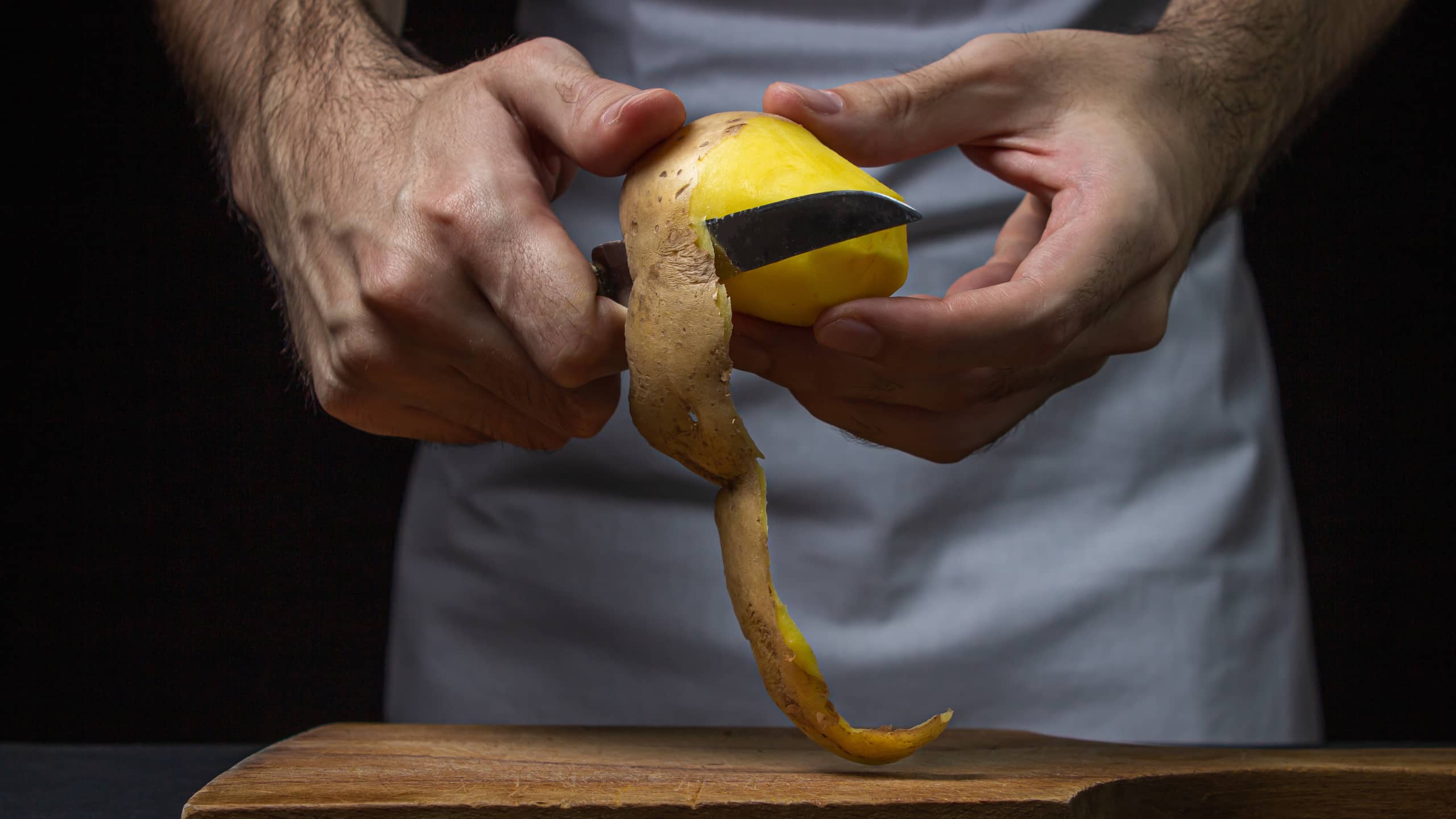 Mãos masculinas descascando uma batata com uma faca.