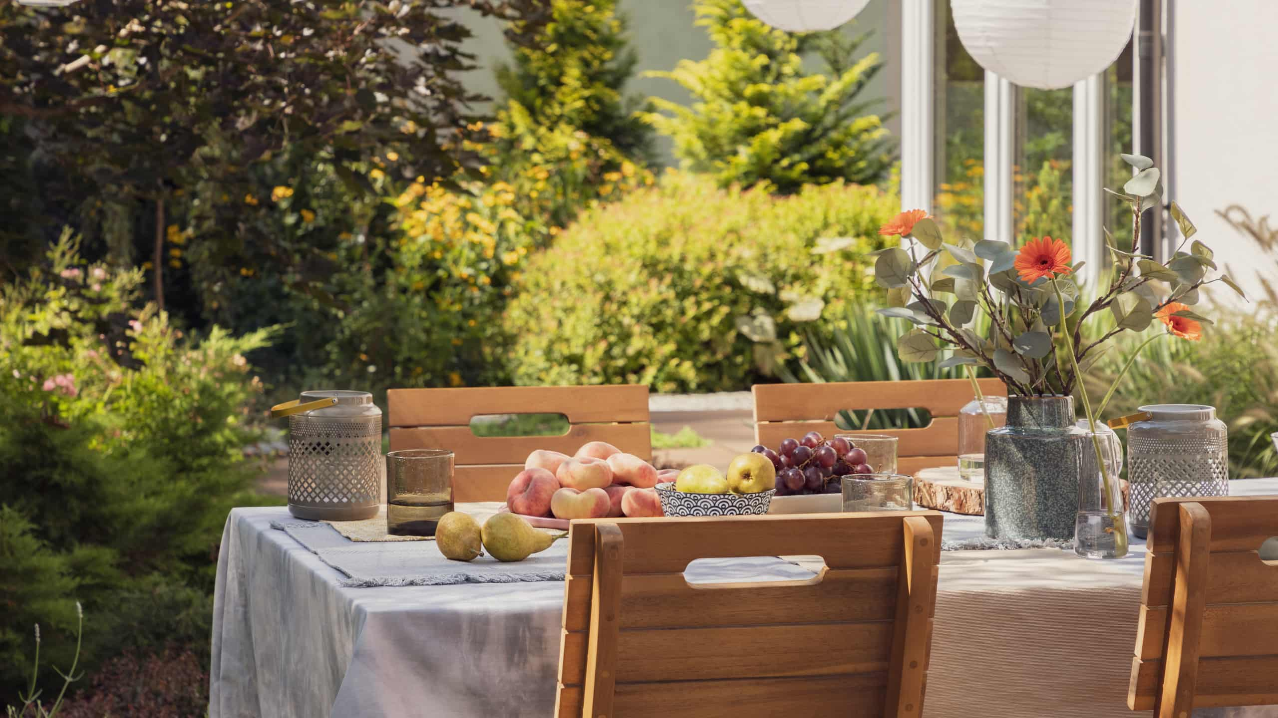 Mesa e cadeiras postas no exterior, com pratos e tigelas com fruta e um jarro com flores silvestres.