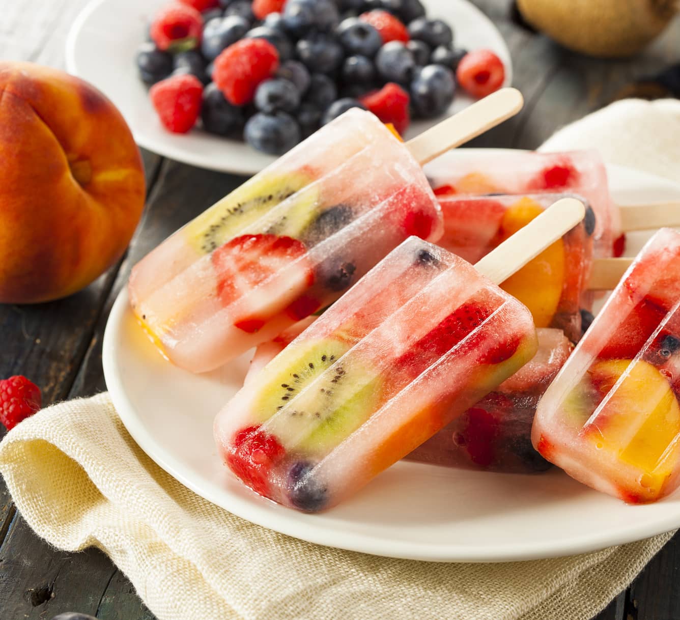 Gelados de pauzinho com frutas em pedaços (quivi, morango, mirtilo).