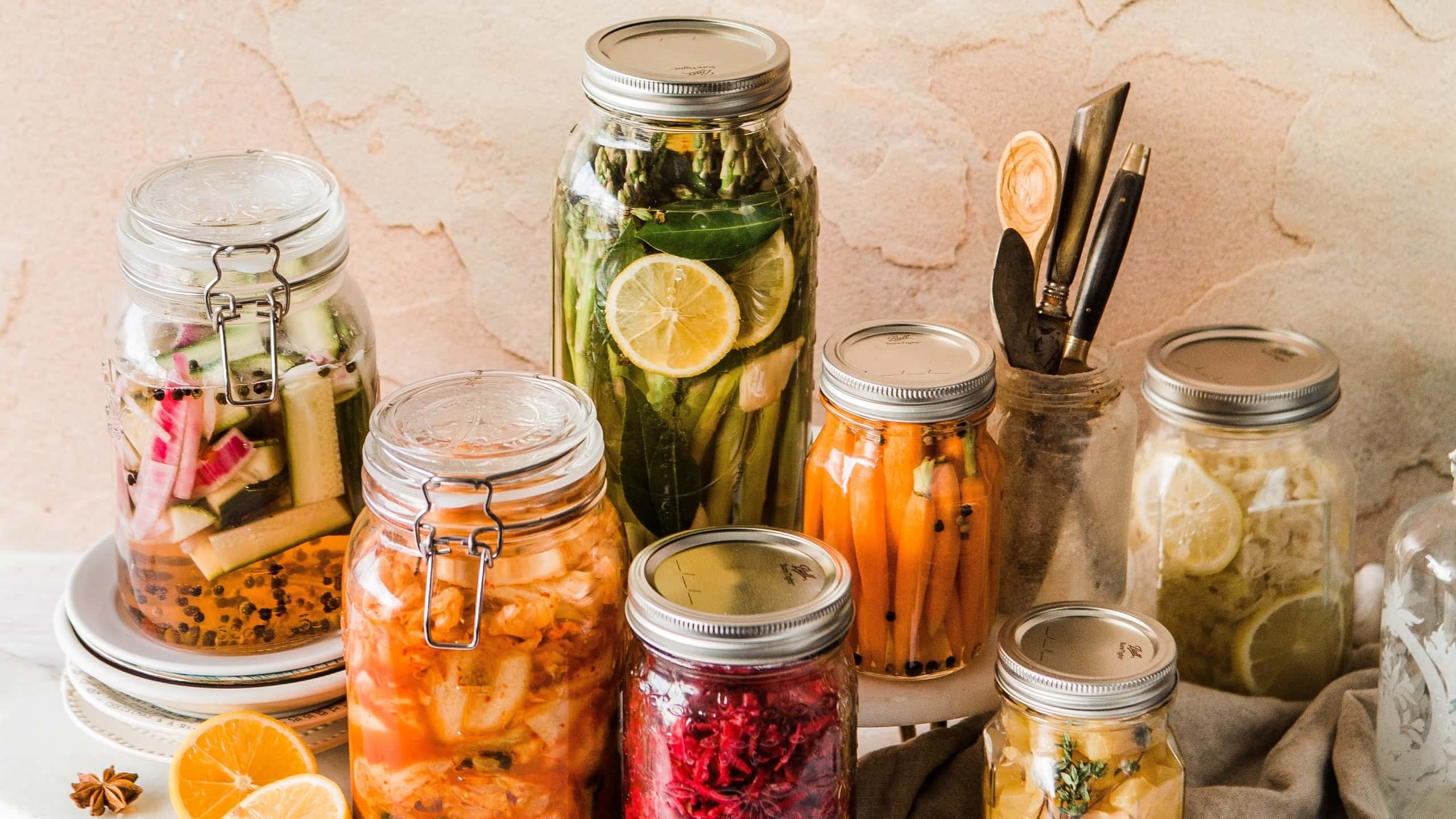Mason jars with several pickles (cucumber, asparagus, carrots, kale) on a kitchen counter.