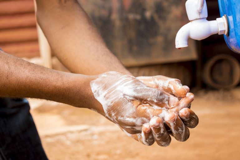 Person soaping hands, close to an outdoor tap.