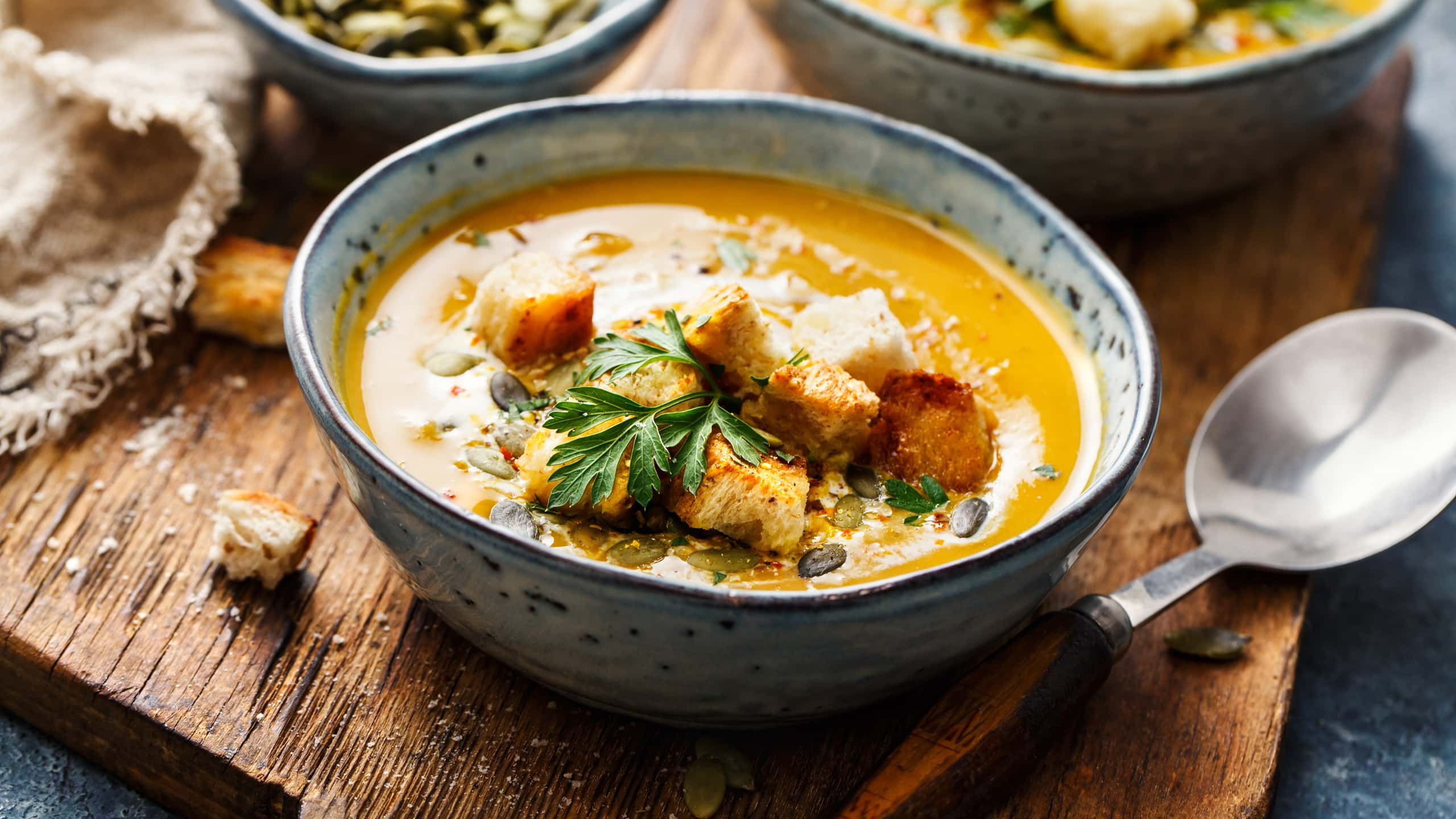 Tigela rústica com sopa servida com sementes e croutons, em tábua envelhecida.