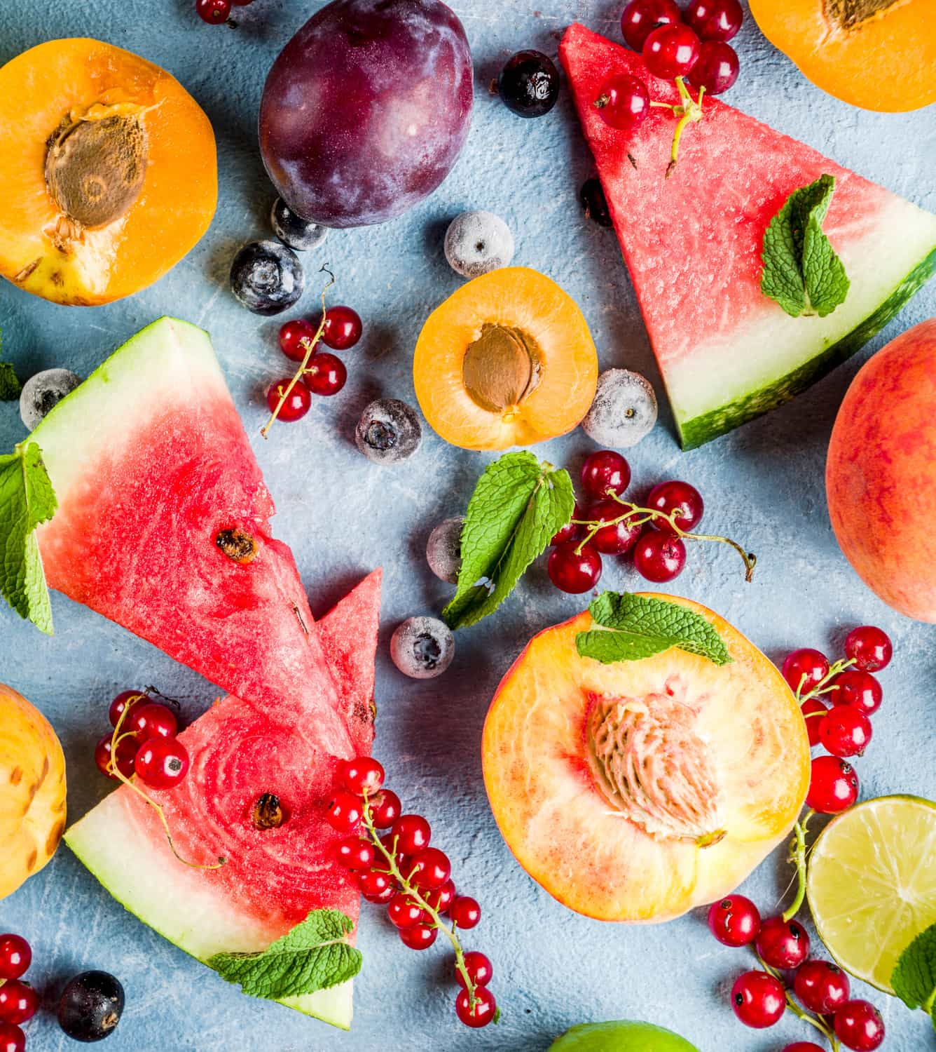 Sliced watermelon and peach spread over a table and decorated with berries.