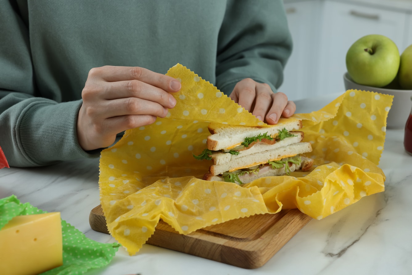 Men wrapping a sandwich in bee's wrap, on a cutting board.