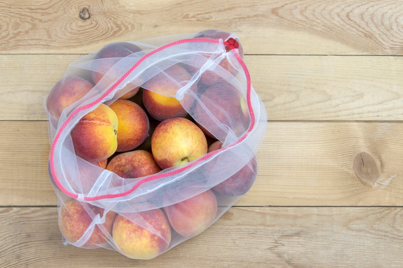 Open net bag with peaches on a wooden table.