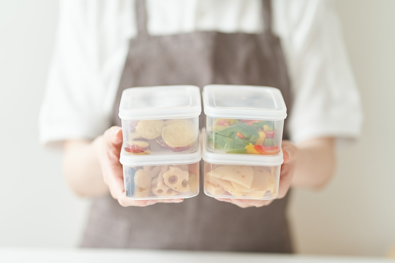 Person holding four reusable containers with food.