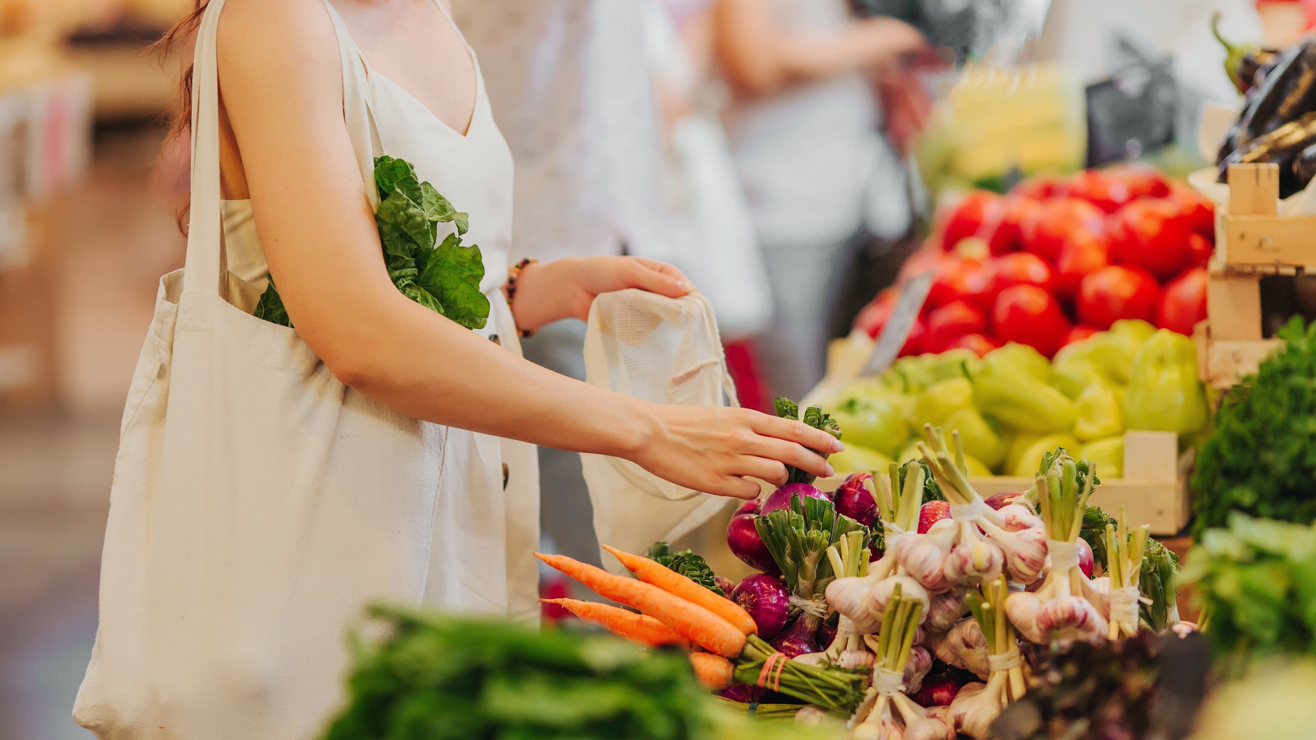 Woman picking vegetables in a market, using cloth bags.