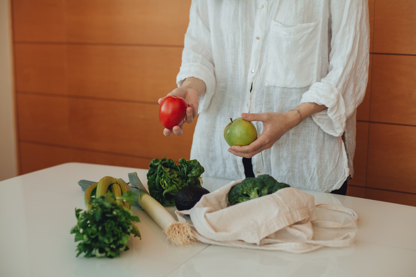 Woman taking fruit and vegetables out of a cloth bag and putting them in a table.