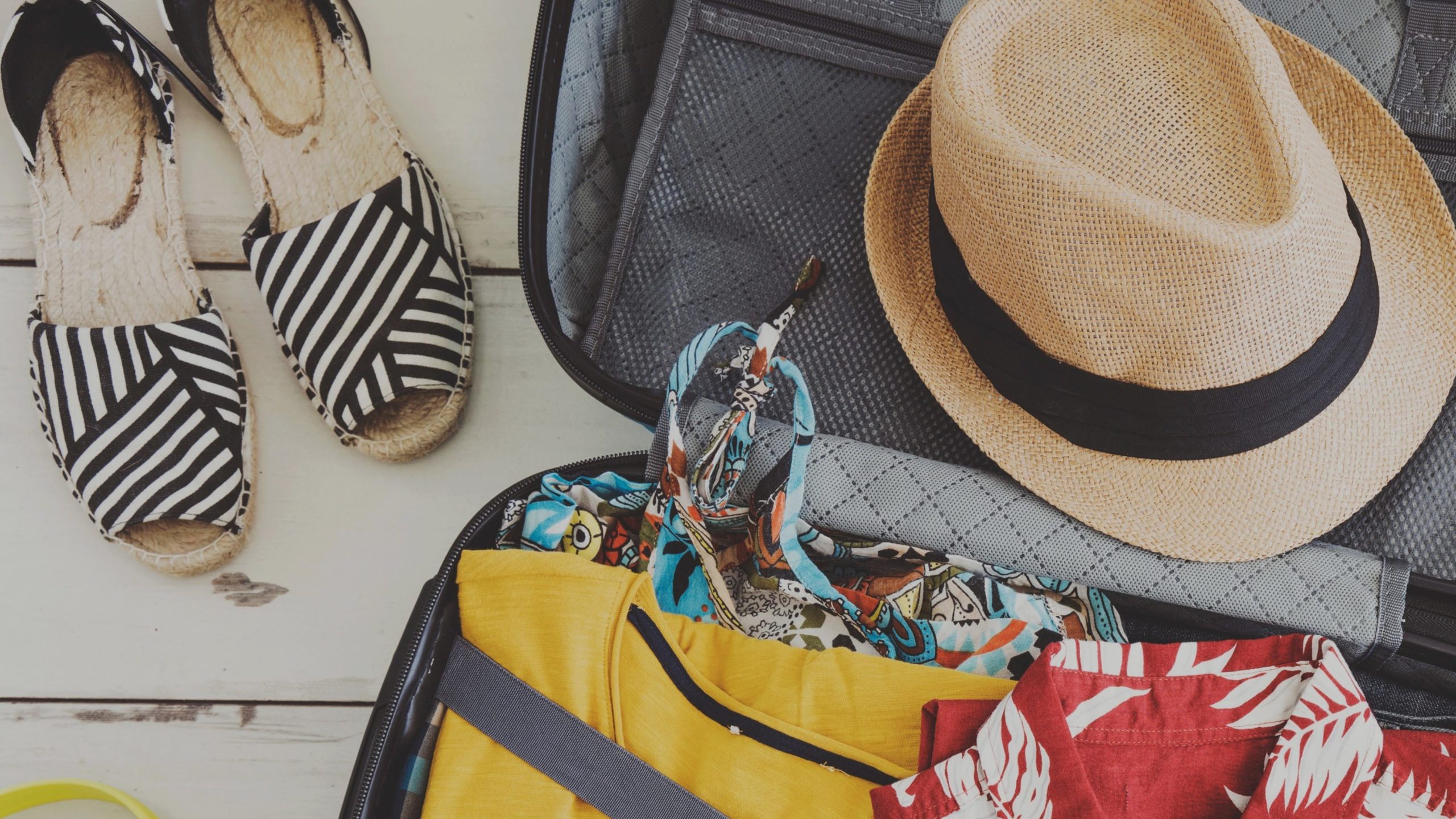 Sandals and open suitcase with summer clothes and a straw hat.