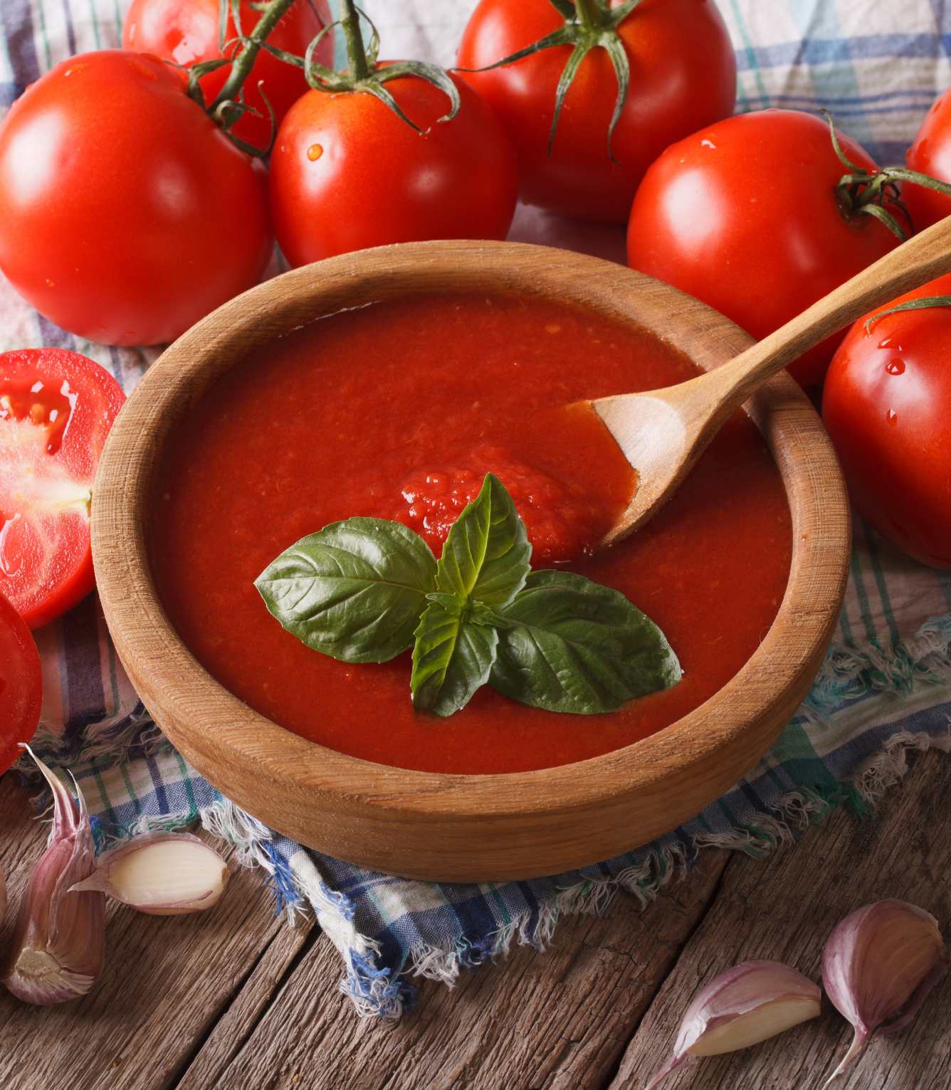 Wooden bowl with homemade tomato sauce, and several whole and sliced tomatoes spread on a kitchen cloth.