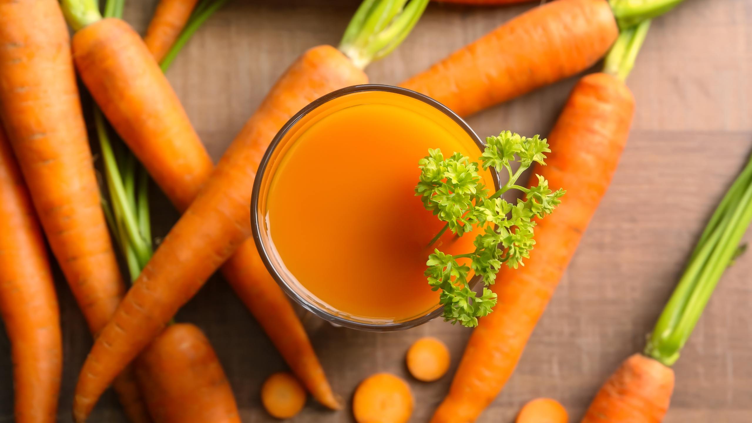 Glass of carrot juice, decorated with a branch, and several carrots scattered in a table.