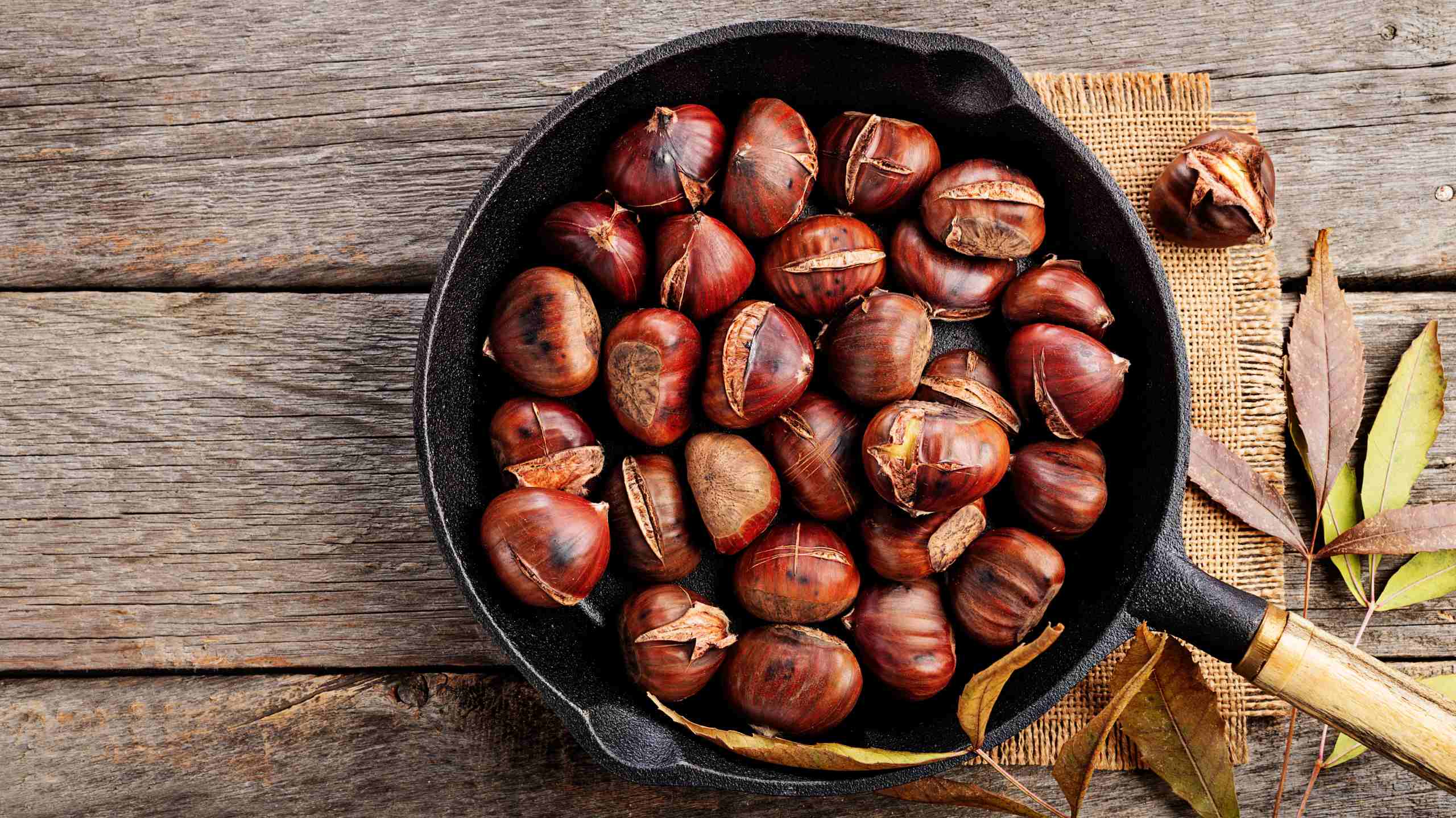 Chestnuts roasted in a cast iron frying-pan, over a burlap cloth, in a wooden table.