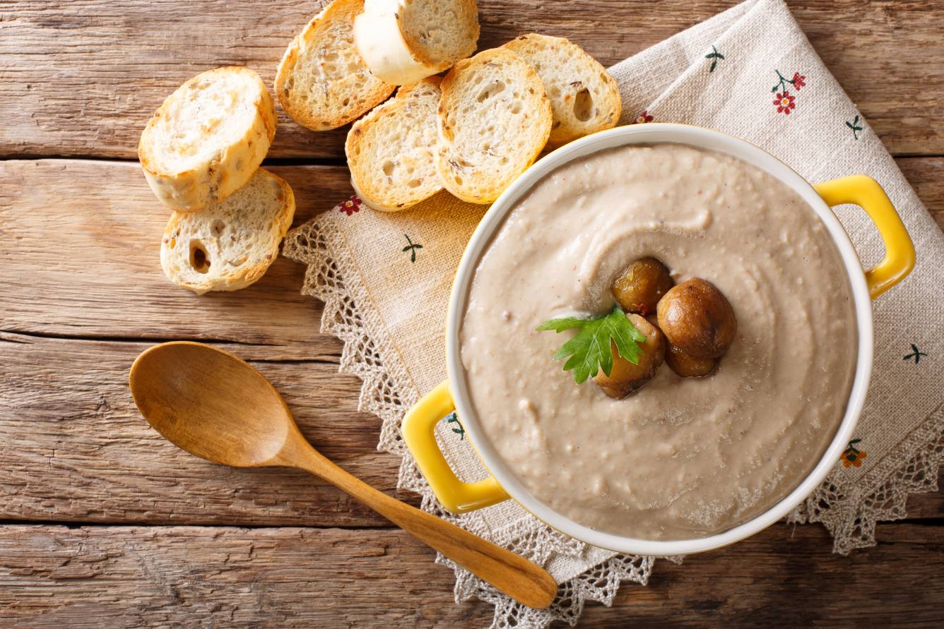 Chestnuts soup bowl, served with sliced bread, over a decorated cloth in a wooden table.