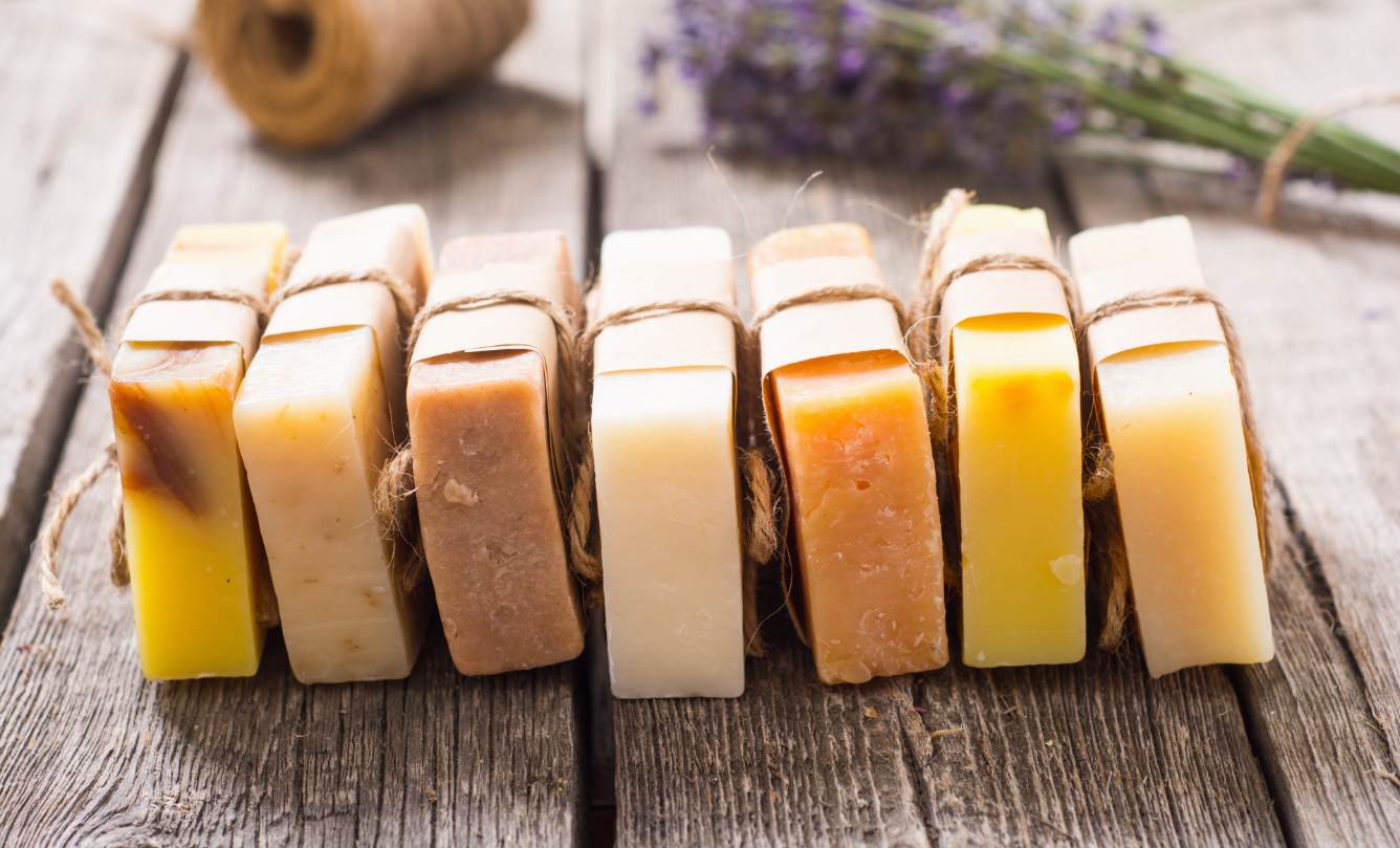 Several homemade soaps aligned in an old wood table, with a branch of lavender.