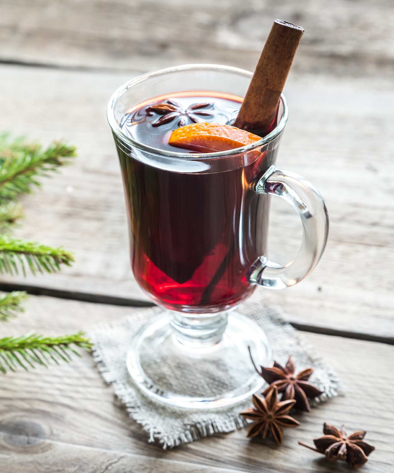 Tall glass cup with Scandinavian Glögg aromatised with a cinnamon stick, an orange slice and star anise.