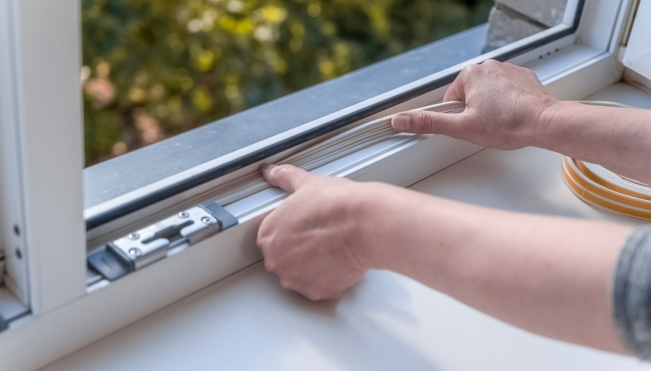 Hands applying insulating foam tape in a window.