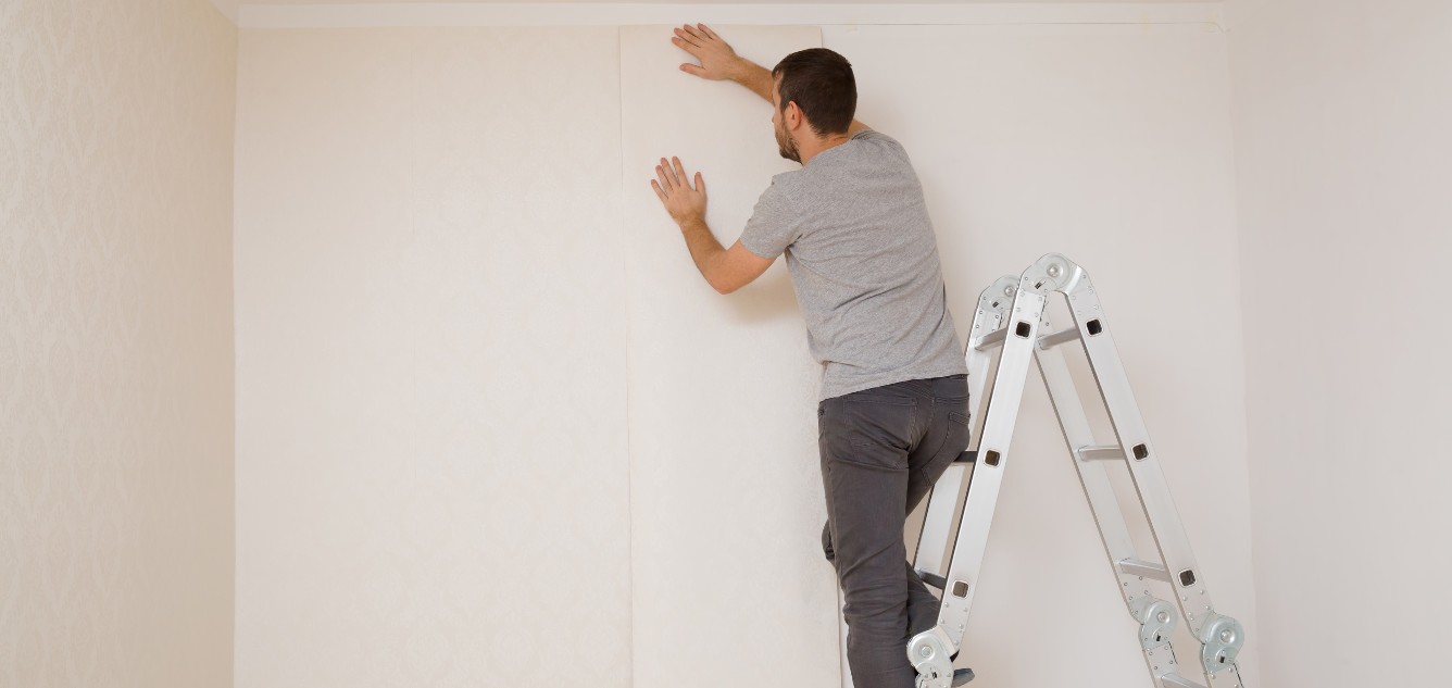 Man in a ladder applying insulating wallpaper.