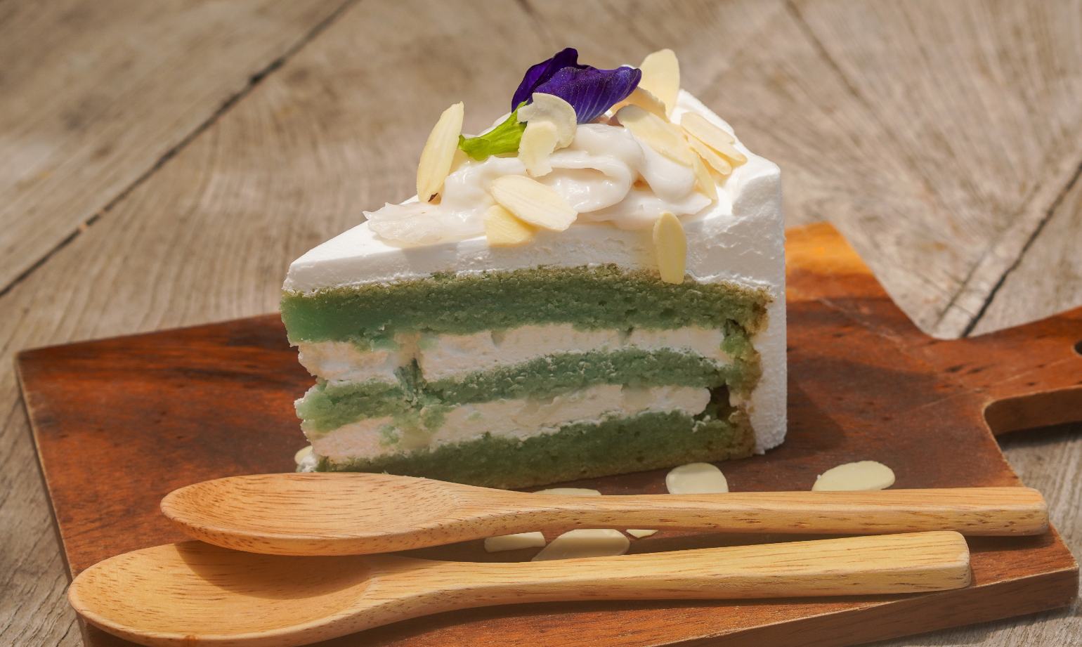Slice of a pea and vanilla cake with laminated almonds, on a wooden cutting board.