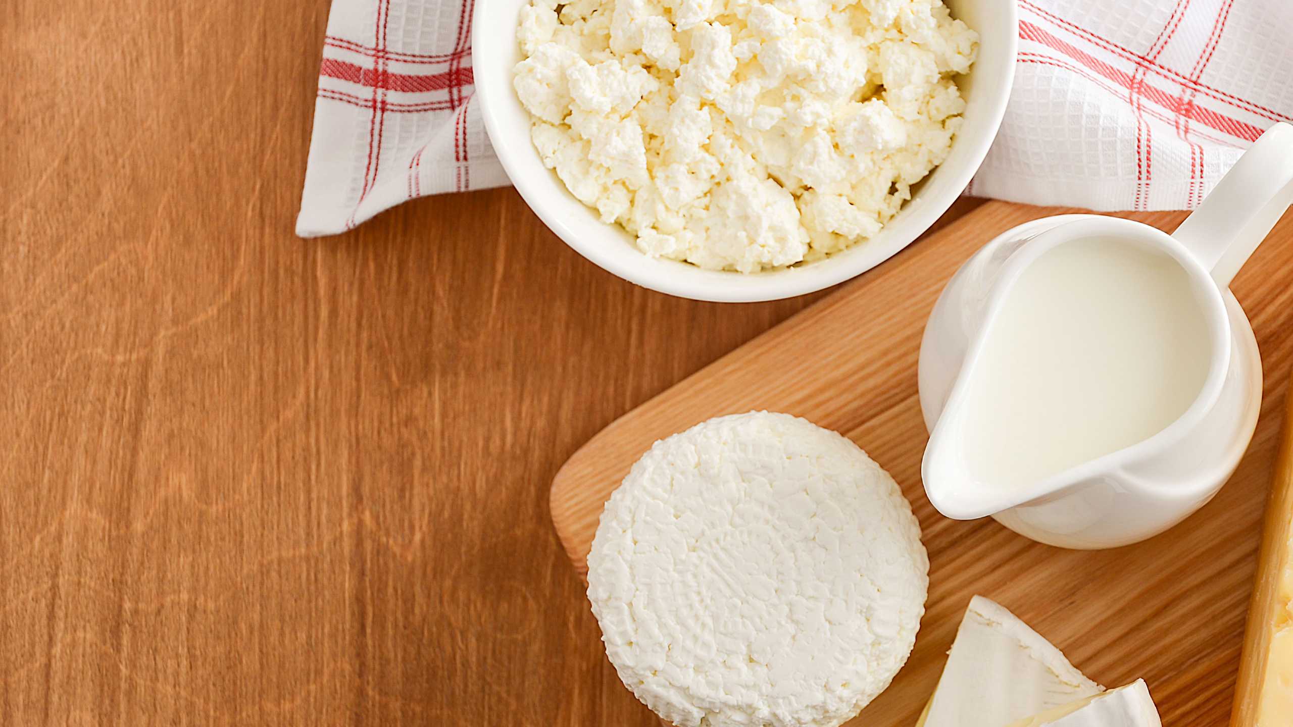 Several dairy products over a wooden table: cottage cheese, cheese, milk.