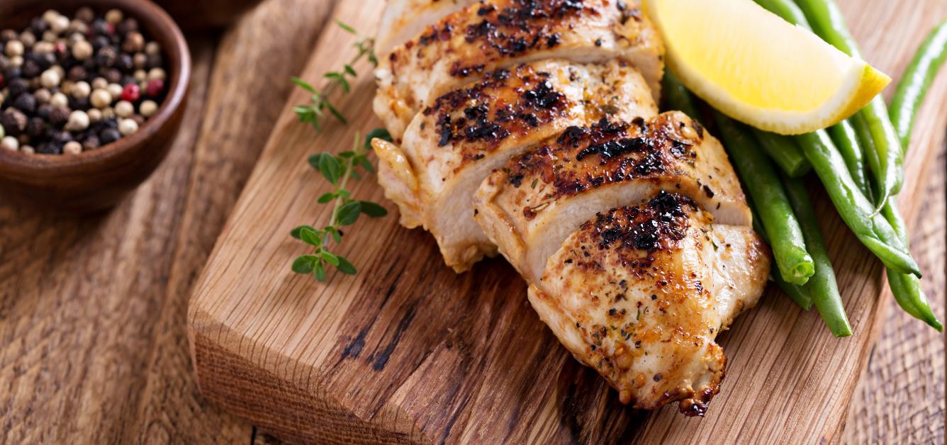 Grilled chicken breast, sliced, over a wooden board.