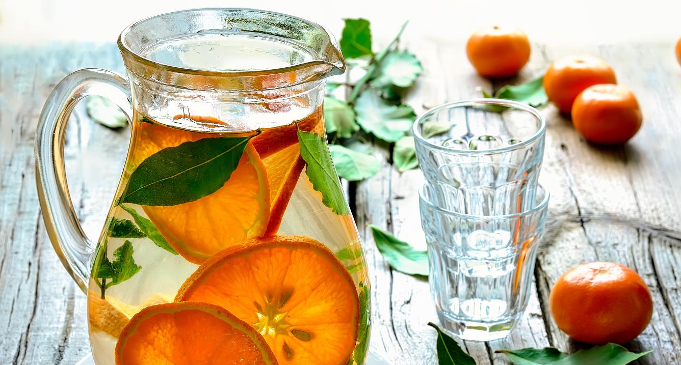 Glasses and jar with orange infused water, on a wooden table.